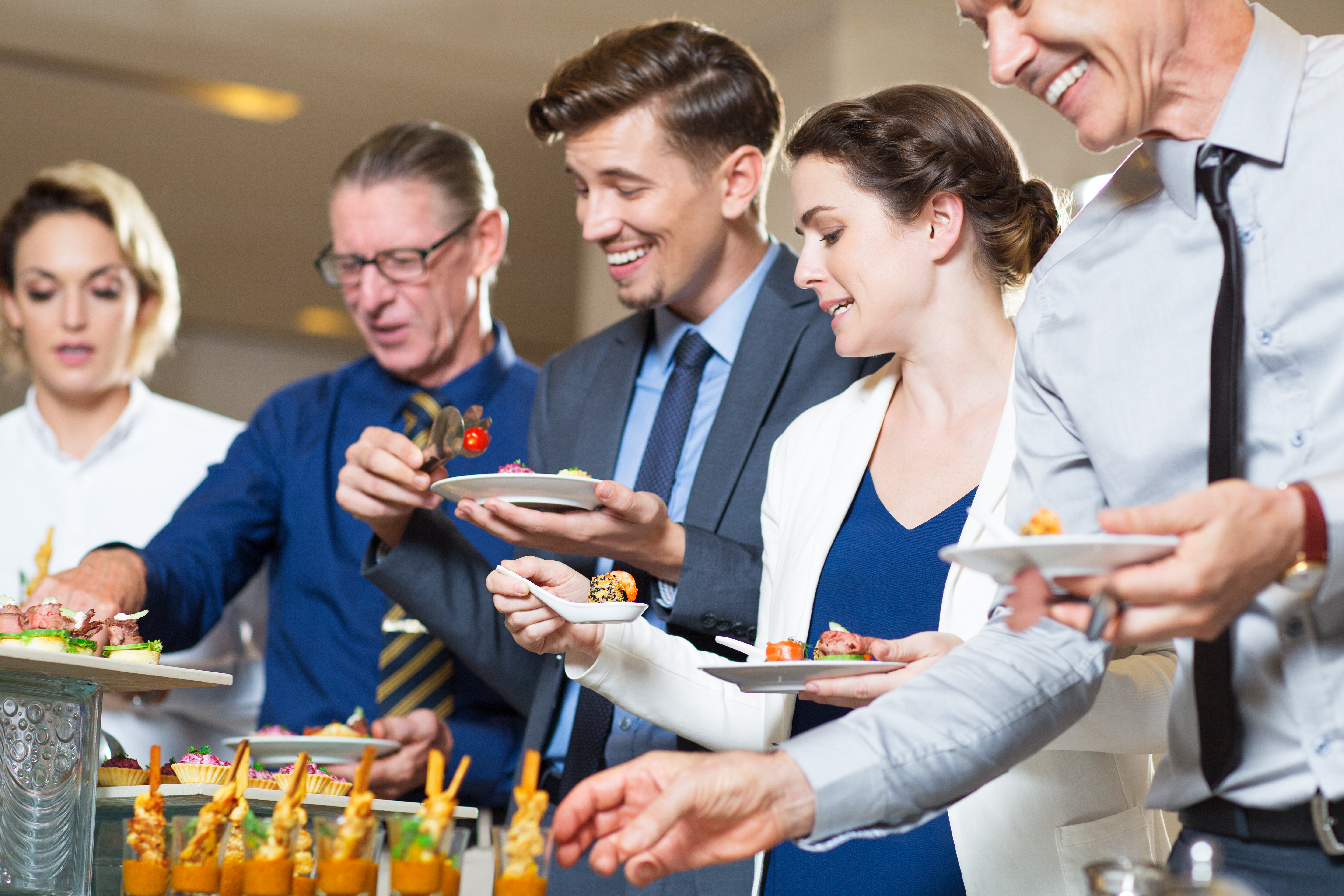 Group of five business people standing in buffet of restaurant and serving themselves with snacks. Catering concept